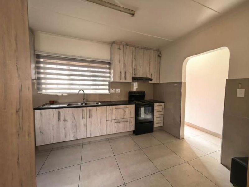 A functional kitchen featuring light wood-look cabinetry, a double sink, tiled flooring, and a built-in extractor fan with a freestanding stove.