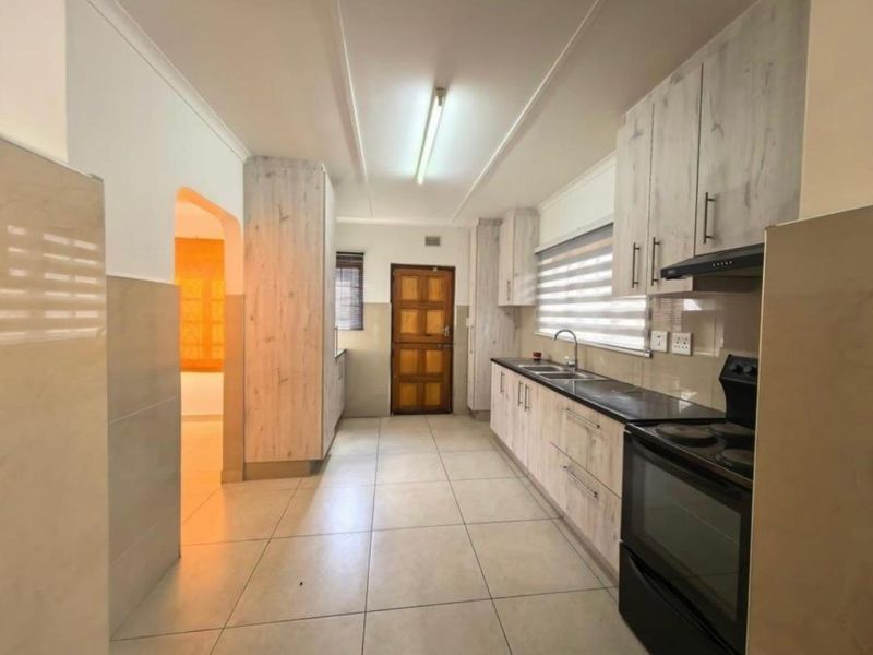 A functional kitchen featuring light wood-grain cabinetry, tiled flooring, a double sink, and a built-in electric stove with an extractor fan.