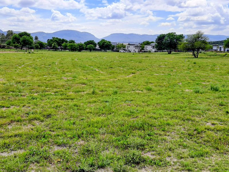 A large, open, undeveloped plot of land featuring a grass lawn and distant mountain views.