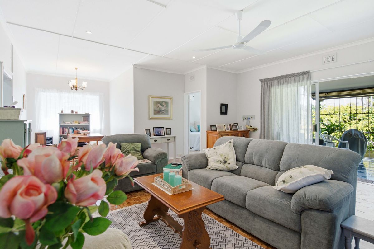 A bright and spacious living room featuring parquet flooring, a ceiling fan, and direct access to an outdoor patio area through sliding glass doors.