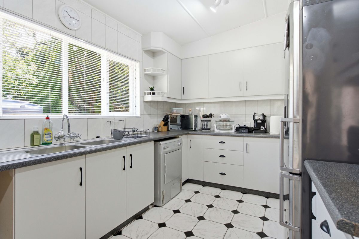 A functional kitchen featuring white cabinetry, laminate countertops, a double stainless steel sink, and classic tiled flooring with a backsplash.
