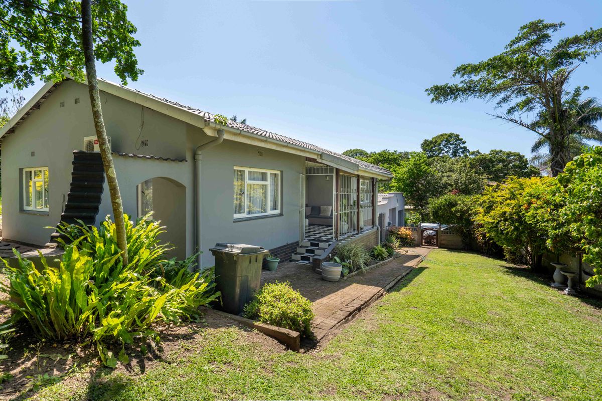 Rear view of the house featuring a paved patio area, established garden, and secure access to the main living space.