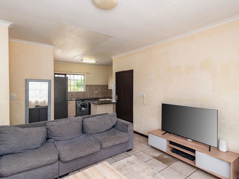 Open-plan living area featuring tiled flooring and an adjoining kitchen space with built-in cabinetry and granite countertops.