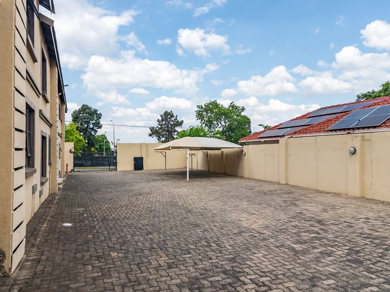 A paved exterior parking area featuring a shade port, perimeter walling, and solar panels installed on the adjacent roof structure.