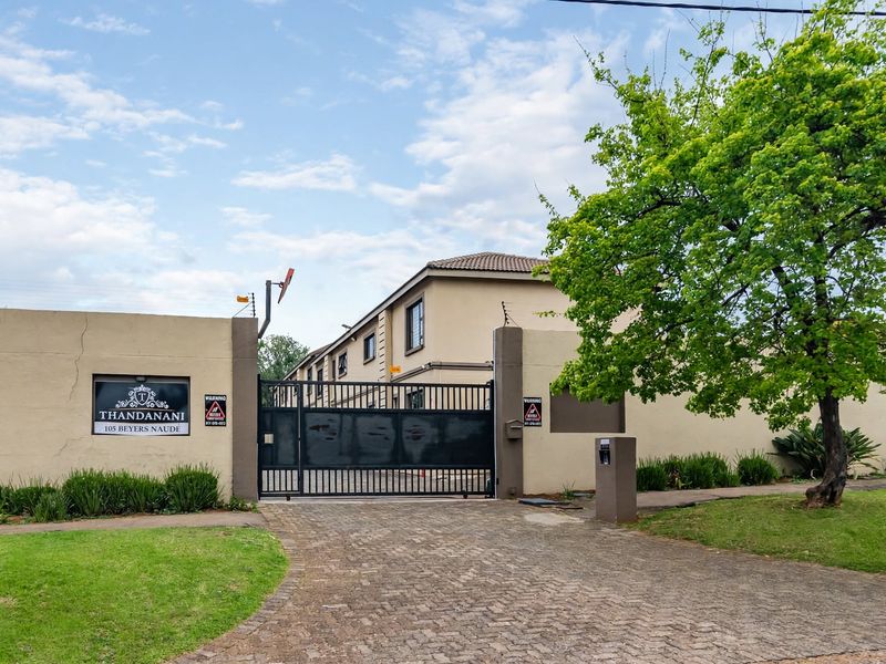 Front entrance view of the Thandanani apartment complex featuring a secure gated driveway, perimeter wall with electric fencing, and established landscaping.