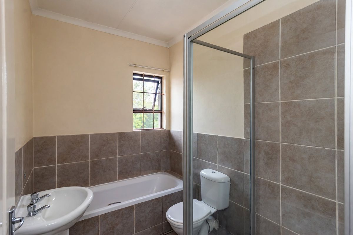 A functional bathroom featuring a pedestal basin, built-in bathtub, and a separate shower enclosure with neutral wall tiling.