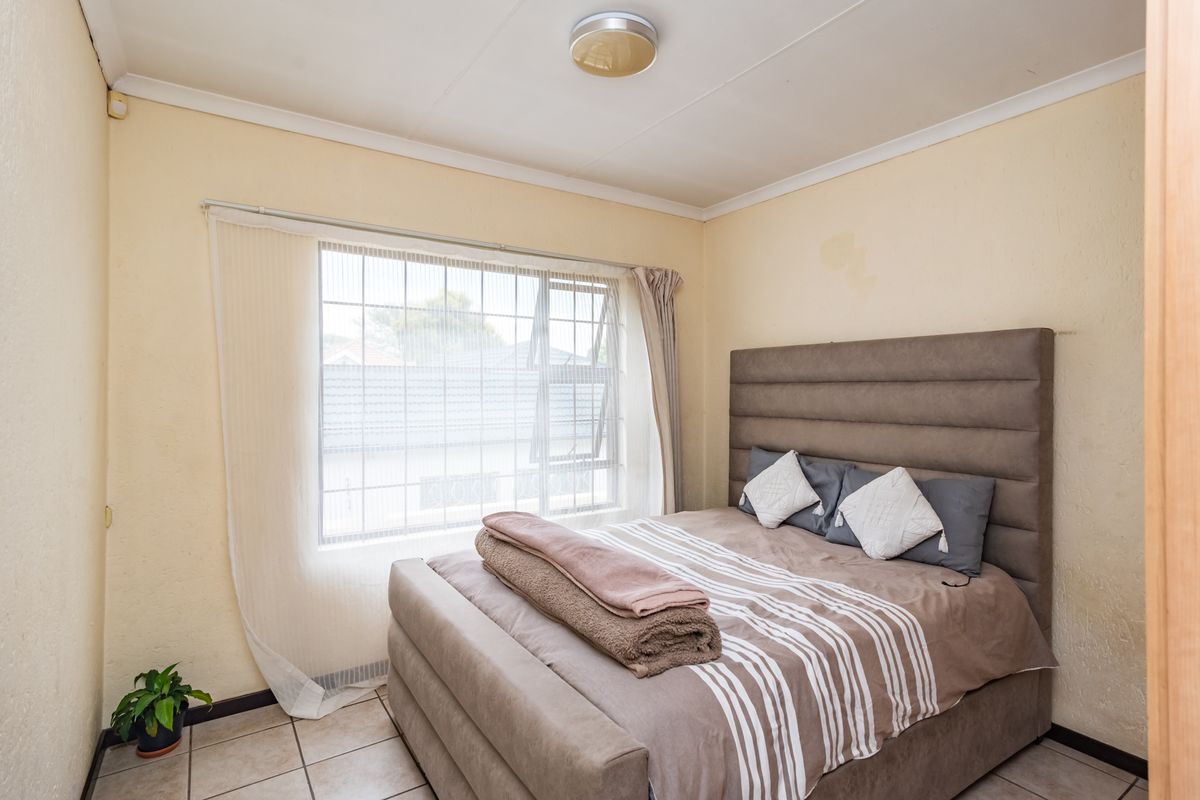 A functional bedroom featuring tiled flooring, a window with security bars, and a coved ceiling, providing a comfortable and practical living space.