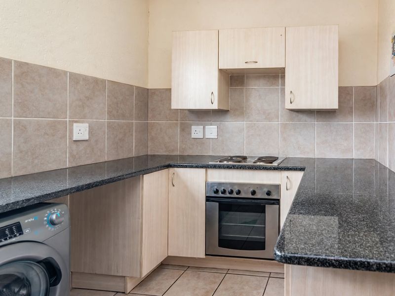 A functional kitchen featuring granite countertops, built-in oven, electric hob, tiled backsplash, and ample cabinetry for storage.