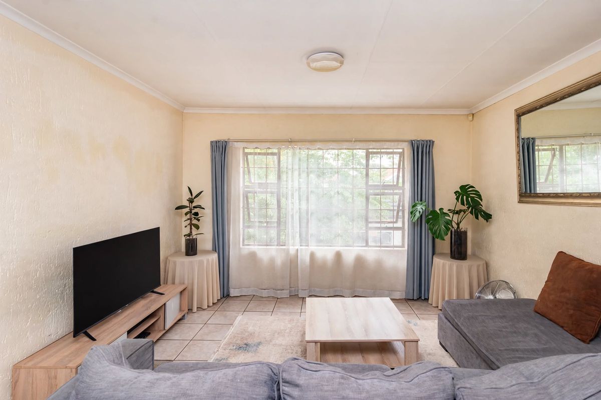 A living room featuring tiled flooring and a large window with security bars. The space requires cosmetic updates to address wall staining and texture.
