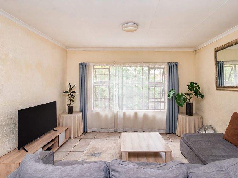 A living room featuring tiled flooring and a large window with security bars. The space requires cosmetic updates to address wall staining and texture.