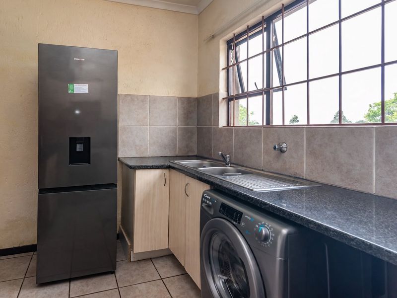 Functional laundry area featuring granite countertops, a stainless steel sink, tiled backsplash, and built-in cabinetry with space for appliances.