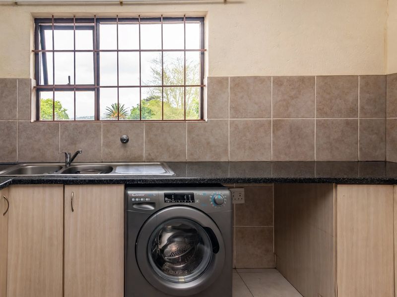 Functional laundry area featuring laminate cabinetry, granite countertops, a stainless steel sink, and tiled backsplash with a window providing natural light.
