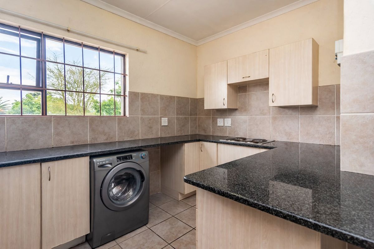 Functional kitchen featuring granite countertops, built-in cabinetry, tiled backsplash, and an integrated electric hob with space for a washing machine.