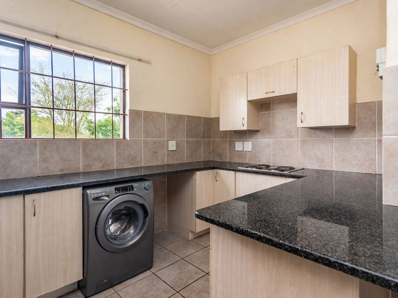 Functional kitchen featuring granite countertops, built-in cabinetry, tiled backsplash, and an integrated electric hob with space for a washing machine.