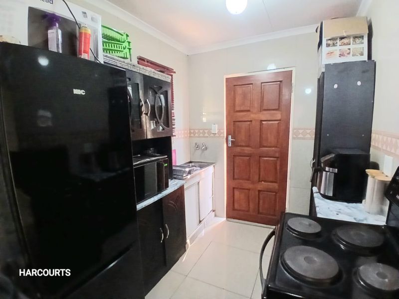A functional kitchen featuring built-in cabinetry, tiled splashbacks, and tiled flooring, providing a practical workspace with direct access to an exterior door.