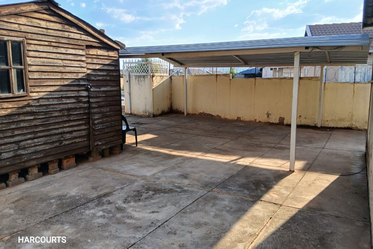 Rear outdoor area featuring a paved patio, a metal carport structure, and a wooden storage shed enclosed by a perimeter wall.