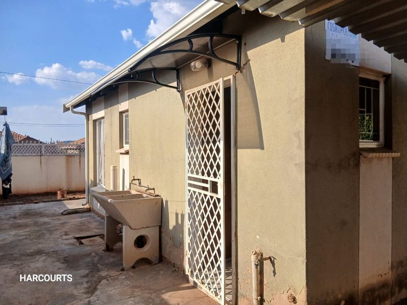 Rear exterior view of the property featuring a concrete laundry sink, security gate, and external plumbing fixtures against a rendered wall.