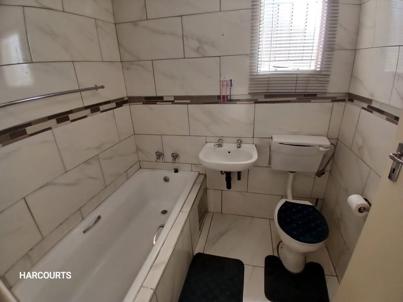 A compact bathroom featuring white marble-look wall tiles, a built-in bathtub, a wall-mounted basin, and a standard toilet.