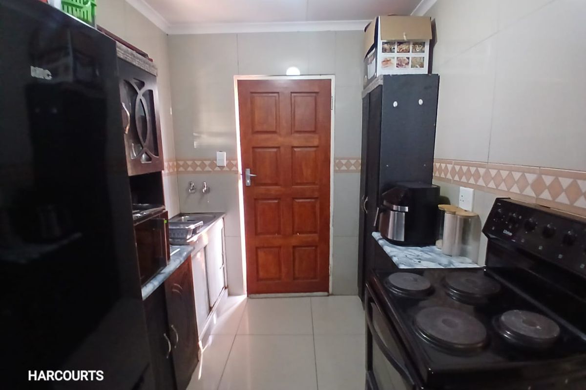 A functional kitchen featuring tiled walls and flooring, built-in cabinetry, a sink, and an electric stove, with a wooden door leading outside.