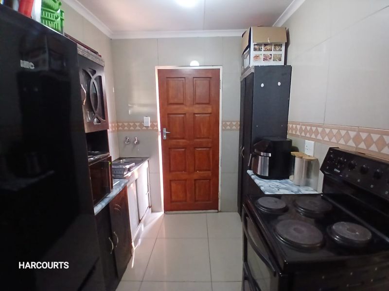 A functional kitchen featuring tiled walls and flooring, built-in cabinetry, a sink, and an electric stove, with a wooden door leading outside.