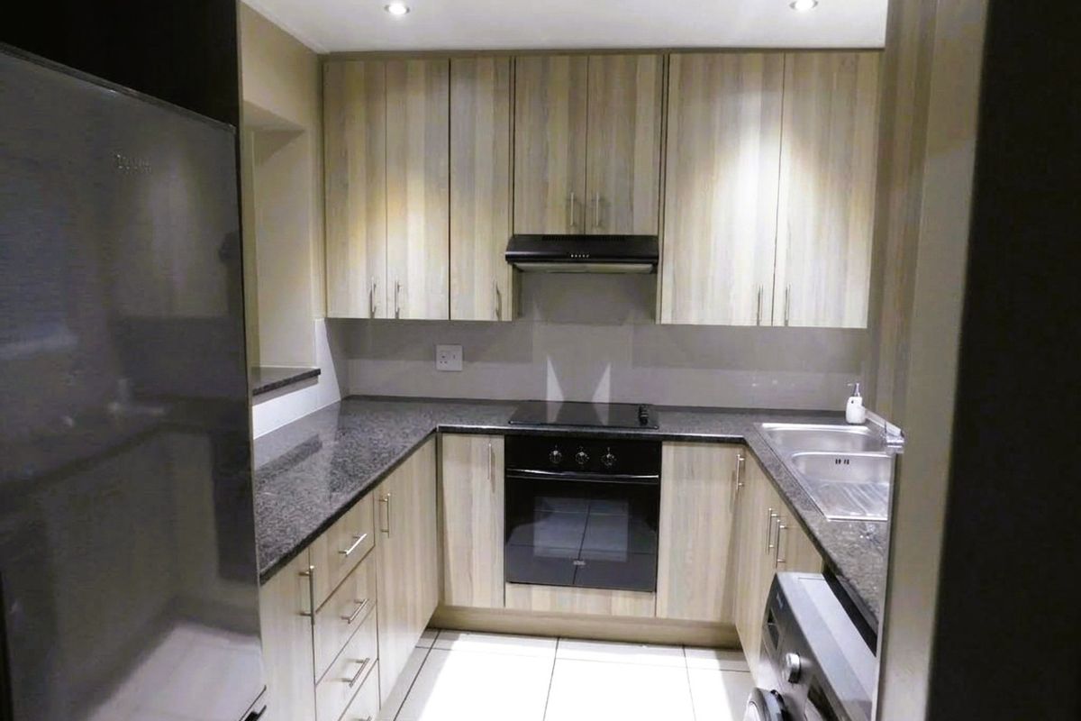 A functional U-shaped kitchen featuring light wood-grain cabinetry, dark granite countertops, integrated oven and hob, and modern tiled flooring.