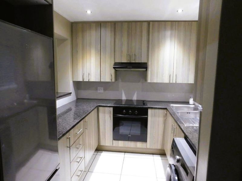 A functional U-shaped kitchen featuring light wood-grain cabinetry, dark granite countertops, integrated oven and hob, and modern tiled flooring.