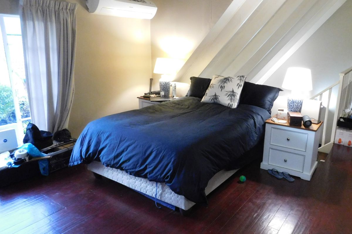 A bedroom featuring dark timber flooring, exposed ceiling rafters, and a wall-mounted air conditioning unit.