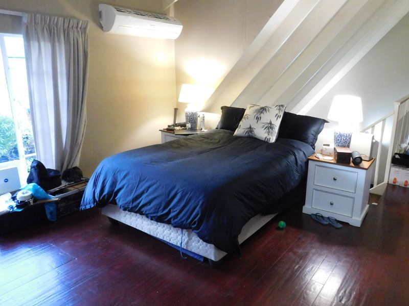 A bedroom featuring dark timber flooring, exposed ceiling rafters, and a wall-mounted air conditioning unit.
