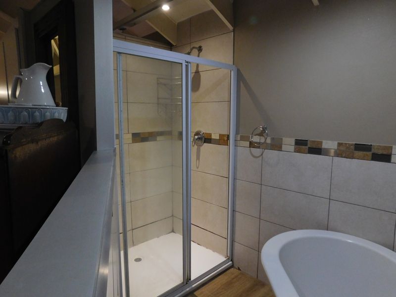 A functional bathroom featuring a glass-enclosed shower, tiled wall accents, and a freestanding bathtub, offering a clean and practical layout.