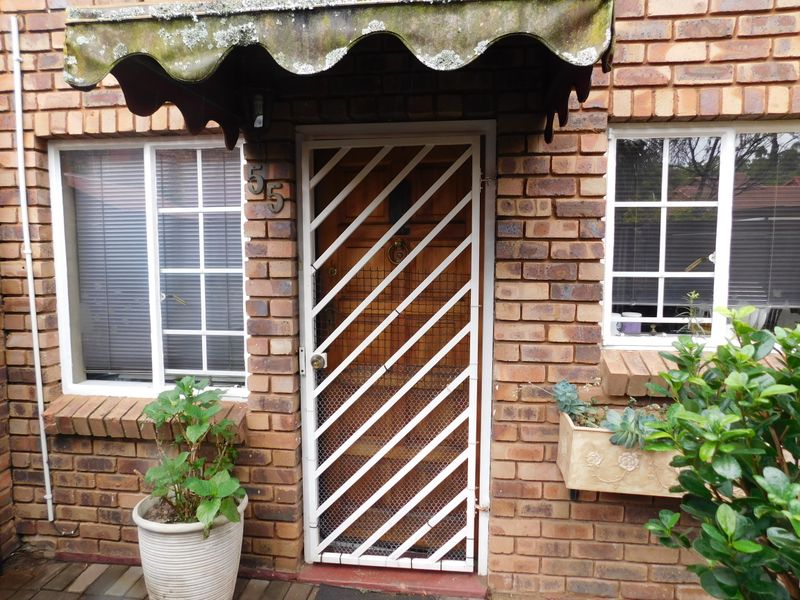 Front entrance of a townhouse featuring a brick facade, a white security gate, and a weathered awning over the doorway.
