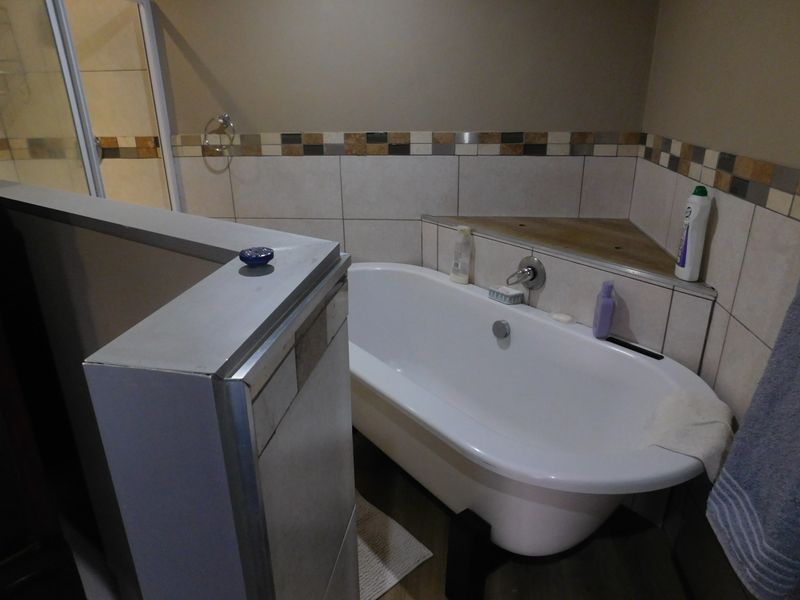 A bathroom featuring a freestanding bathtub, a separate shower enclosure, and neutral wall tiling with a decorative mosaic border.