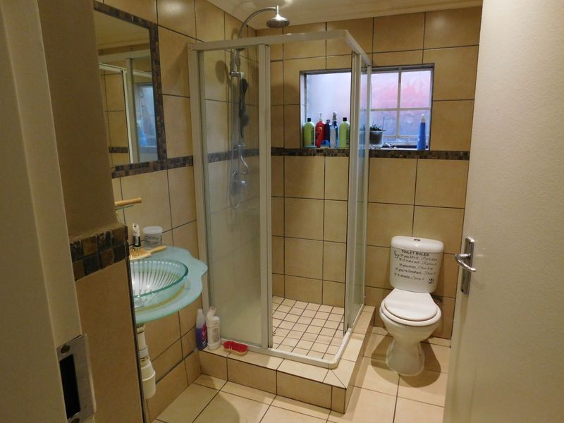 A functional bathroom featuring a glass vessel sink, a corner shower enclosure, and tiled finishes throughout.