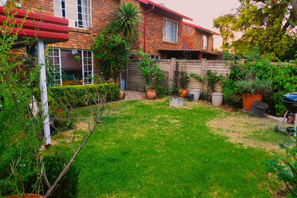 A private rear garden featuring a lawn area, paved pathway, and brick townhouse facade with perimeter timber fencing.