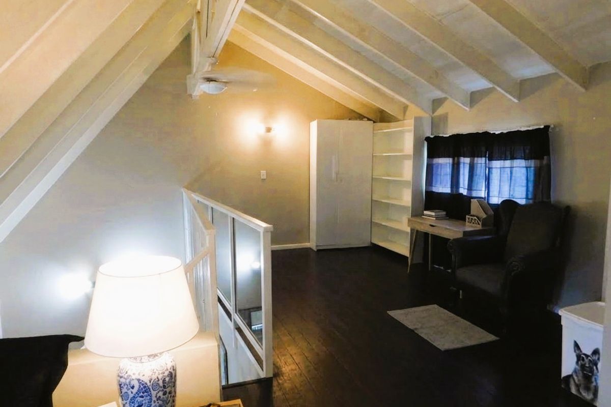 A loft-style living area featuring a vaulted ceiling with exposed timber rafters, dark wood flooring, and a staircase balustrade.