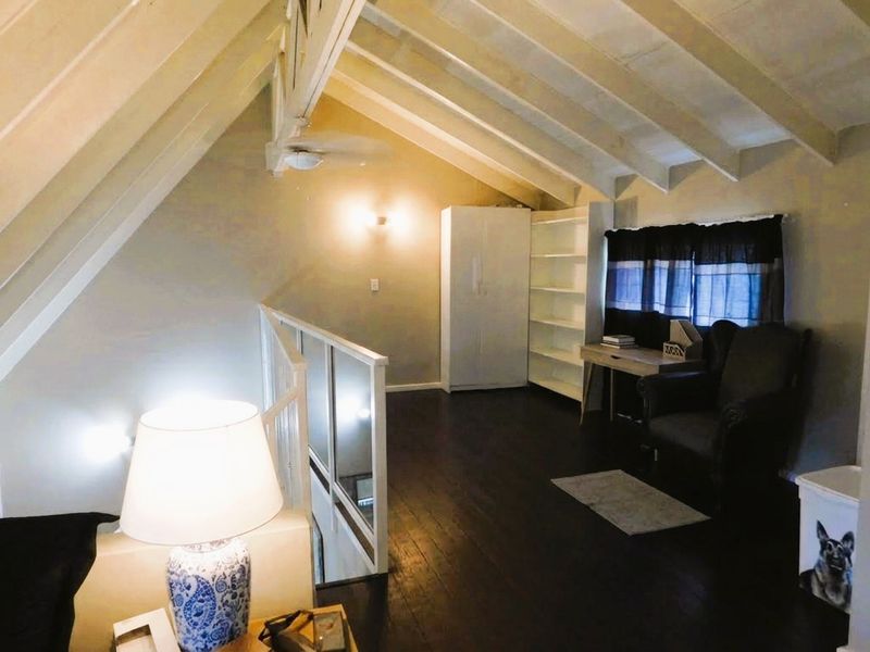 A loft-style living area featuring a vaulted ceiling with exposed timber rafters, dark wood flooring, and a staircase balustrade.