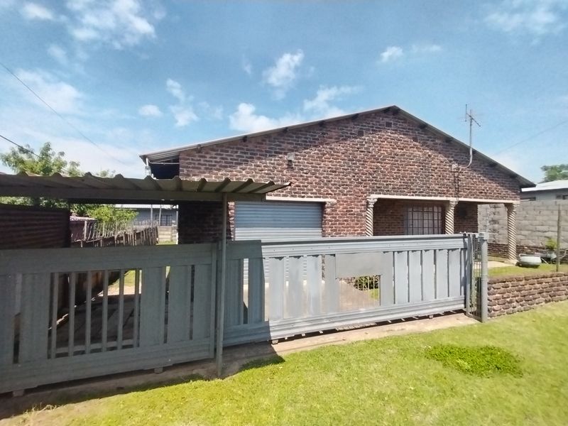 Front view of a face brick house featuring a sliding driveway gate, attached carport, and garage access.