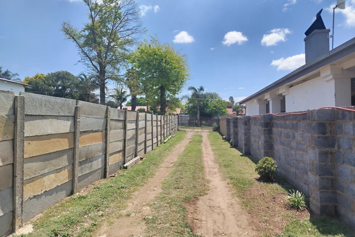 A rear exterior view showing a dirt driveway flanked by precast concrete and cinder block boundary walls leading toward the back of the property.