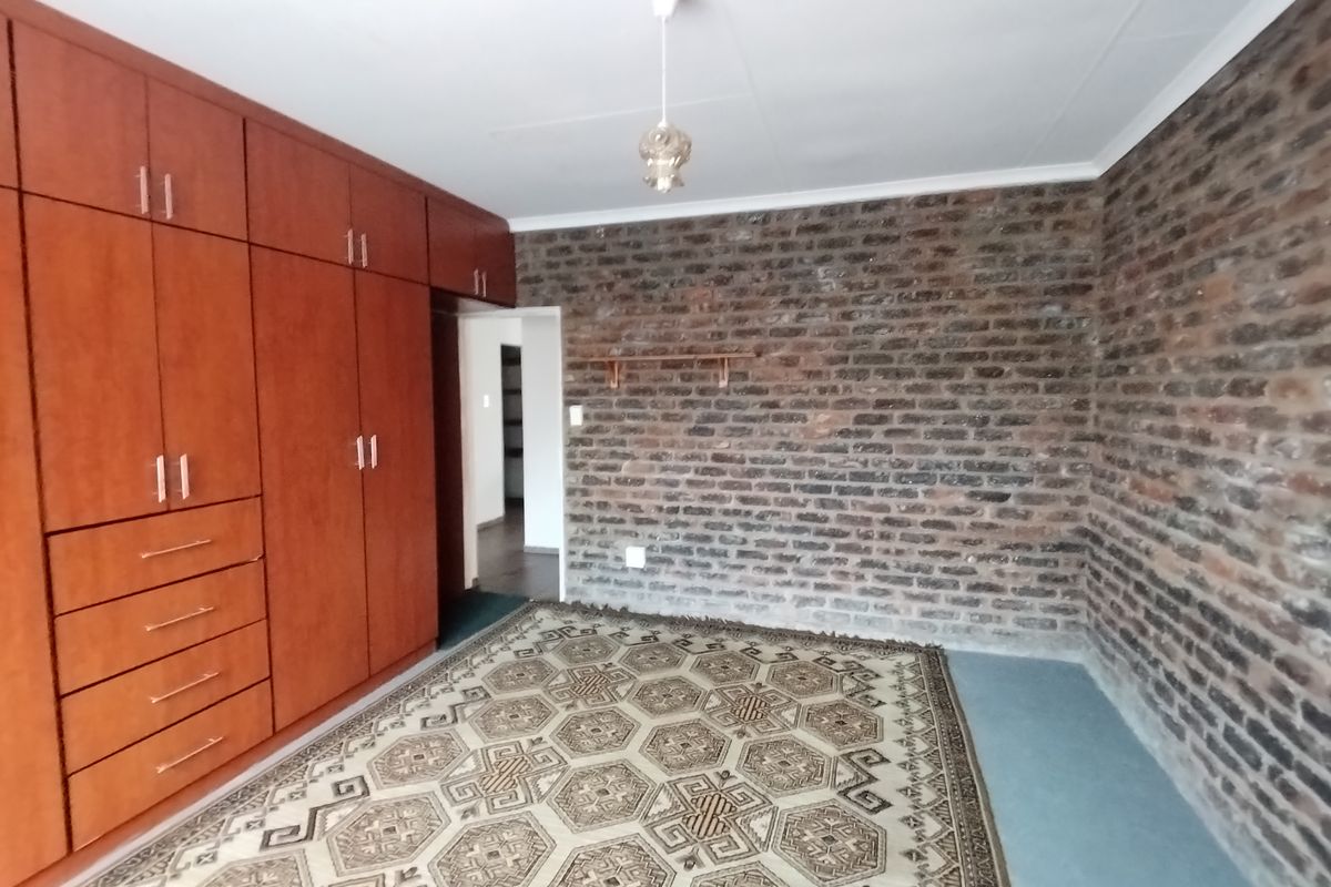 A bedroom featuring a large wall of built-in wooden cupboards and an exposed brick feature wall.
