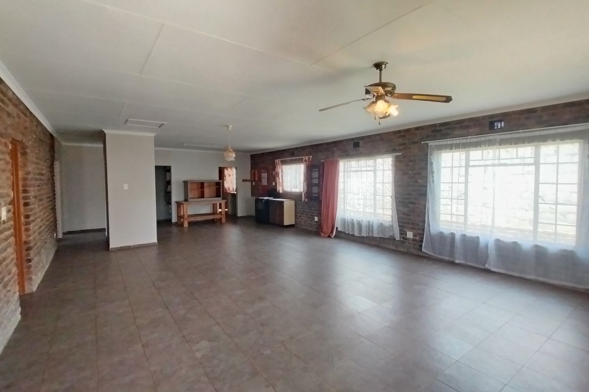 Spacious living area featuring exposed brick walls, tiled flooring, and a ceiling fan, offering a versatile layout with ample natural light.