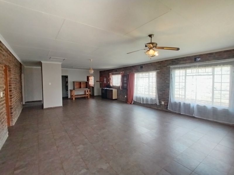 Spacious living area featuring exposed brick walls, tiled flooring, and a ceiling fan, offering a versatile layout with ample natural light.