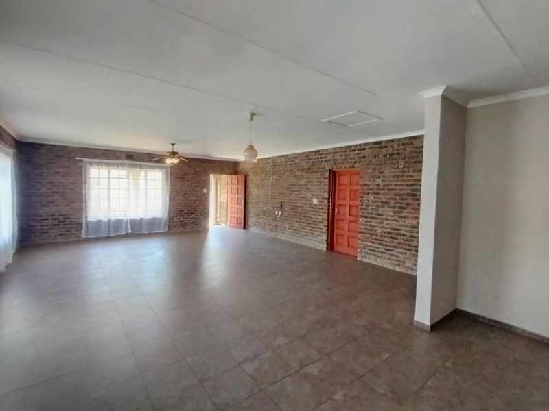 Spacious, empty living area featuring exposed brick walls, tiled flooring, and a ceiling fan, offering a versatile blank canvas for interior design.