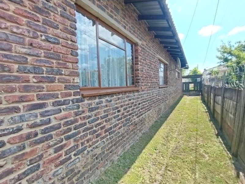 A side view of the property featuring a face brick exterior, steel-framed windows, and a secure boundary wall with razor wire.