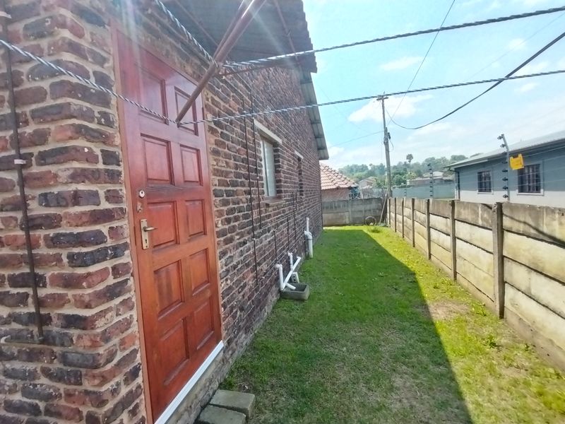 A side view of the property featuring face brick exterior walls, a timber door, and a narrow lawn area enclosed by a precast concrete boundary wall.