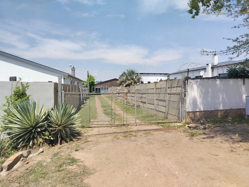 A gated driveway entrance featuring a long gravel path, enclosed by precast concrete boundary walls with security razor wire.