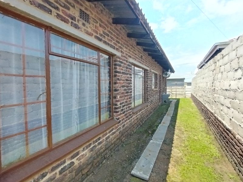 A side view of the property featuring exposed brickwork, large steel-framed windows, and a narrow garden path alongside a boundary wall.