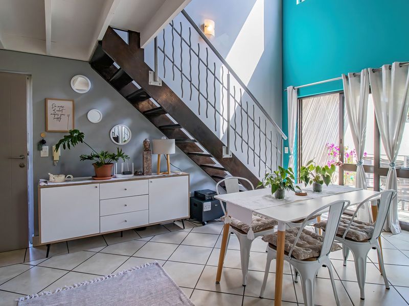 Open-plan living and dining area featuring a striking staircase, tiled flooring, and large sliding glass doors that provide ample natural light.