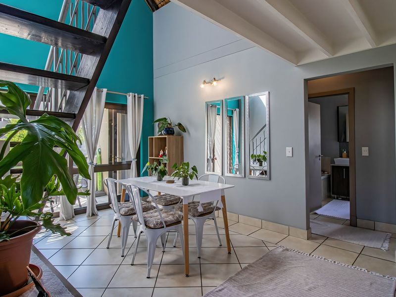 A bright dining area featuring tiled flooring, exposed ceiling beams, and a staircase, with direct access to an outdoor patio through sliding glass doors.