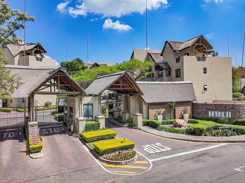 A well-maintained gated security entrance to the Zaleni apartment complex, featuring thatched roof structures, paved driveways, and established landscaped gardens.
