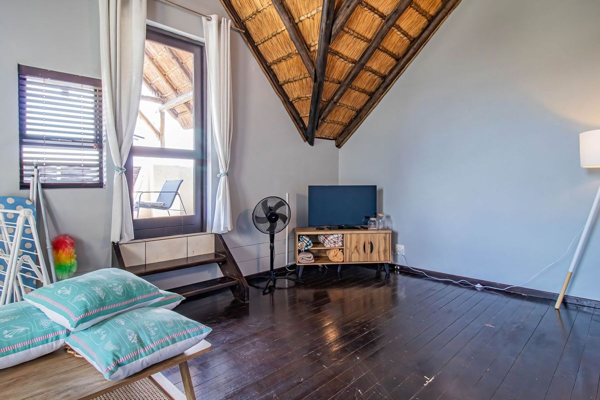 Living area featuring a high vaulted thatch ceiling with exposed timber rafters and dark wood flooring, providing access to an outdoor balcony.