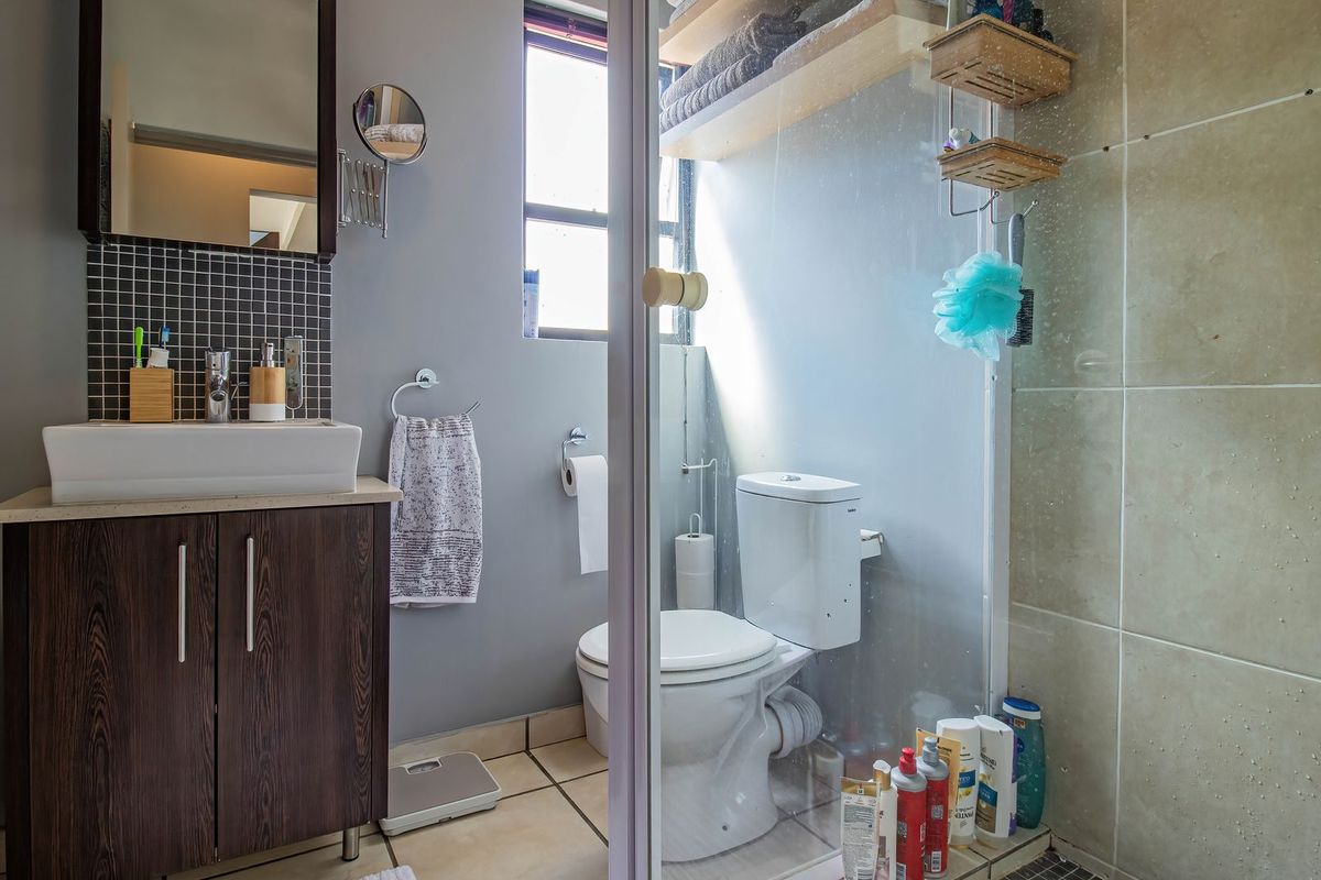 A functional bathroom featuring a dark wood vanity with a vessel sink, mosaic backsplash, toilet, and a glass-enclosed shower with built-in shelving.
